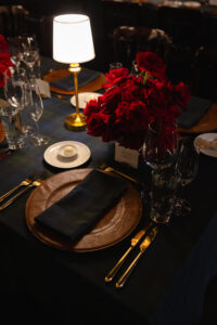 Rehearsal dinner details with leather charger, red roses and gold flatware